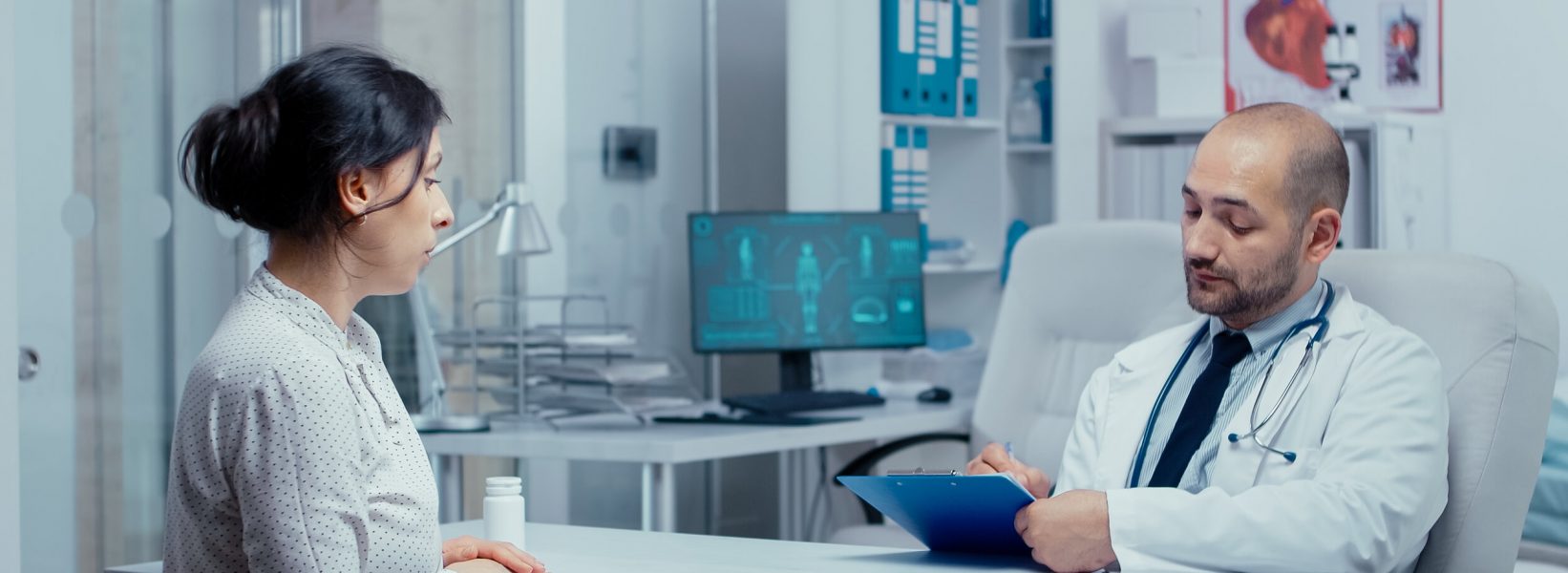Doctor questioning young female patient in his office, writing answears in clipboard. Healthcare in modern hospital or private clinic, disease prevention and consultation in medic office treatment medication diagnosis expertise